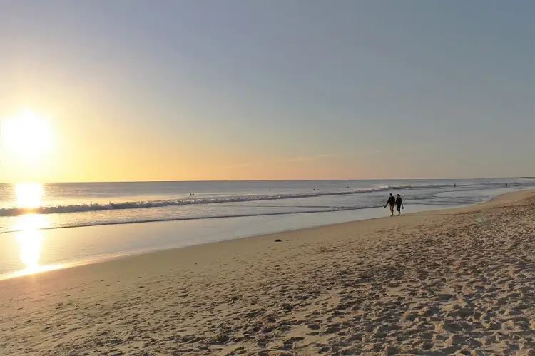 Couple living in Perth walking along Scarborough Beach at sunset.