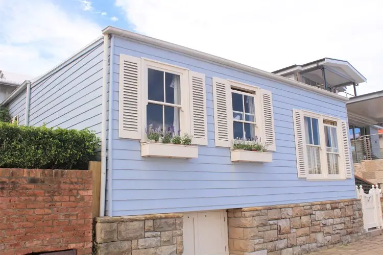 A very cute, baby blue weatherboard home in Watsons Bay, Sydney with shutters and flower boxes.