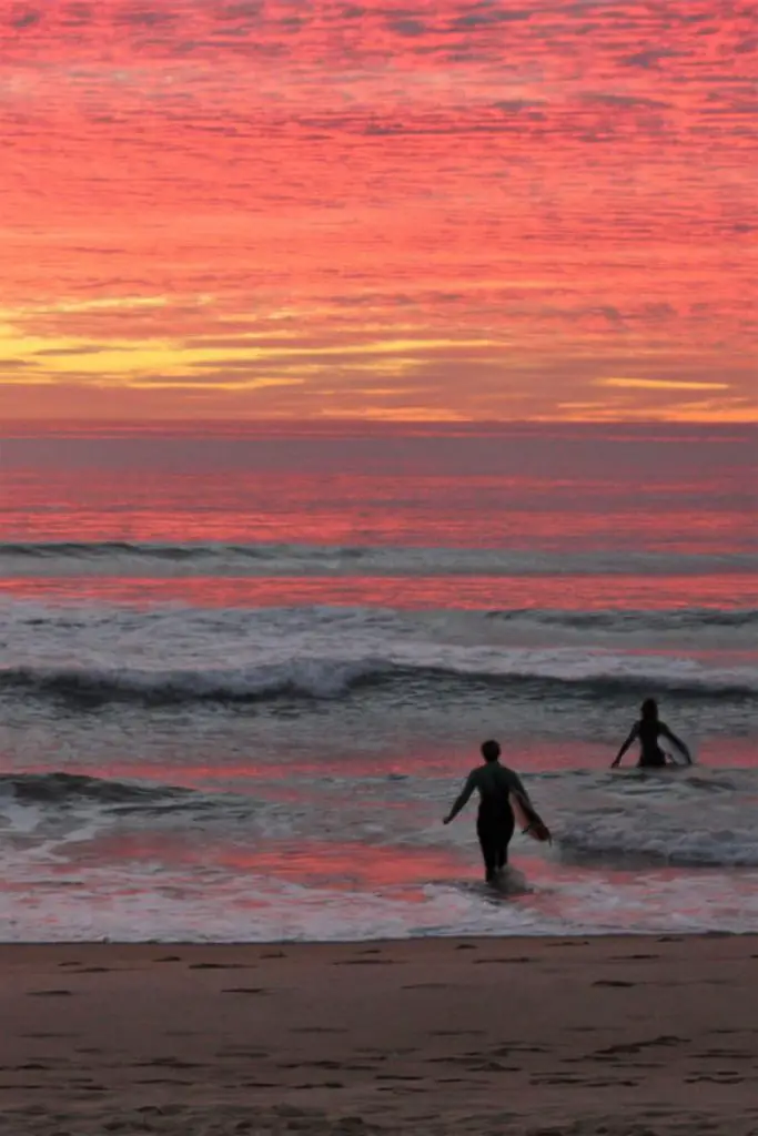 Two surfers underneath a bright red sky at sunrise in Manly, Sydney.