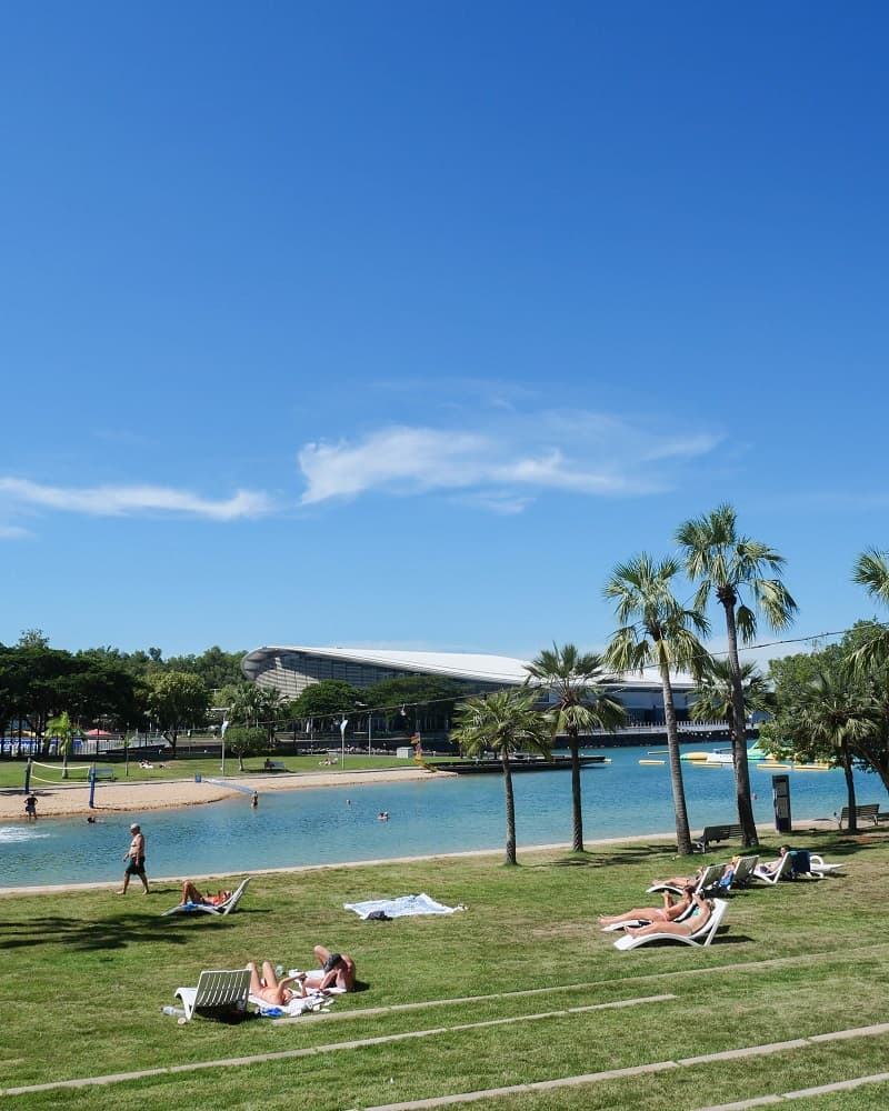 Sunbathers on the grass next to Darwin's city lagoon and manmade beach.